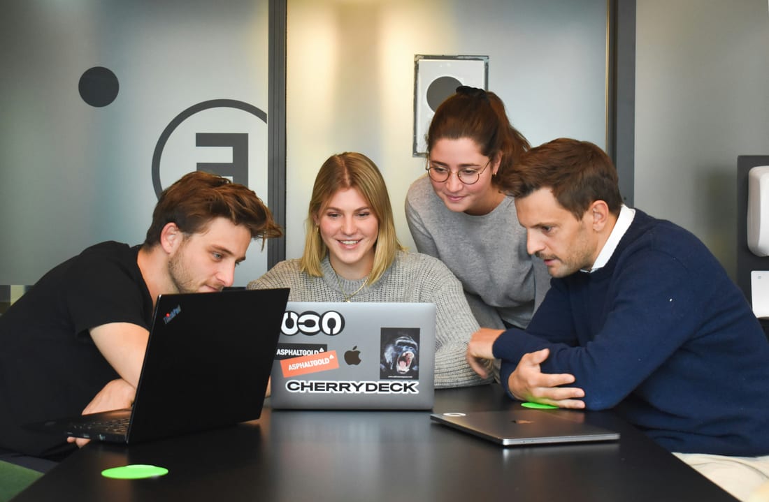 A team of colleagues gathered around a laptop, focused on the screen together